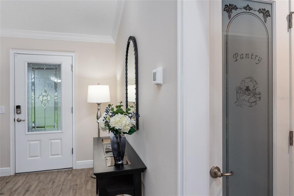 View of FOYER - Front door has 3/4 length, LEADED GLASS insert. Note CROWN MOLDING, 5 1/4' BASEBOARDS, and gorgeous "WOOD LOOK" PORCELAIN TILE FLOORING in LR. To the hallway on R, note CLOSET PANTRY w/ full length, frosted glass insert.