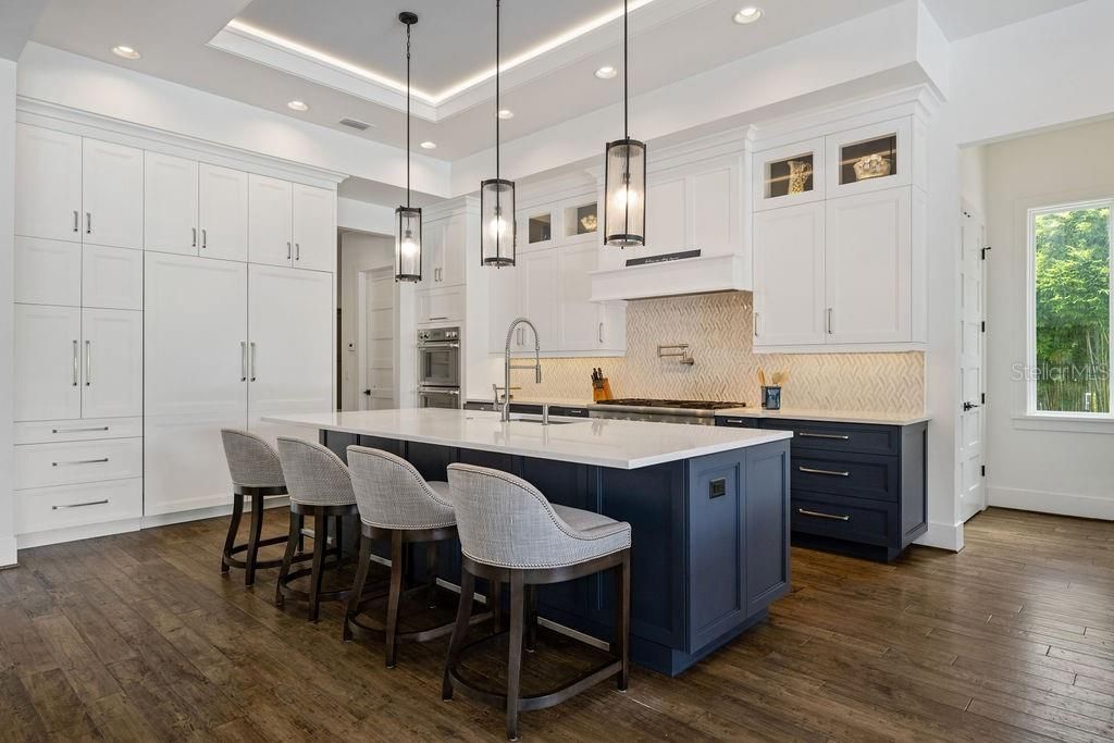 Breakfast bar holds 4 full size bar height stools and gives you a view of custom paneled refrigerator and freezer, wall of cabinetry includes a drawer set.