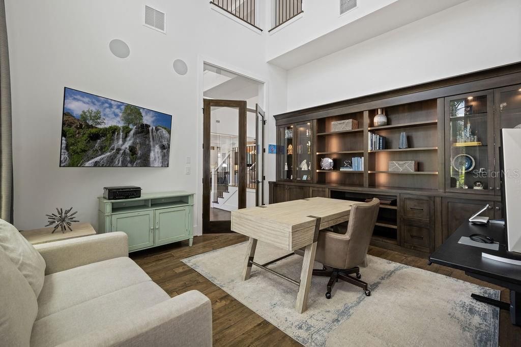 Owners delight in this dedicated office highlighted by a two story coffered ceiling,  privacy via the French doors and plenty of storage in the custom built in shelving system.