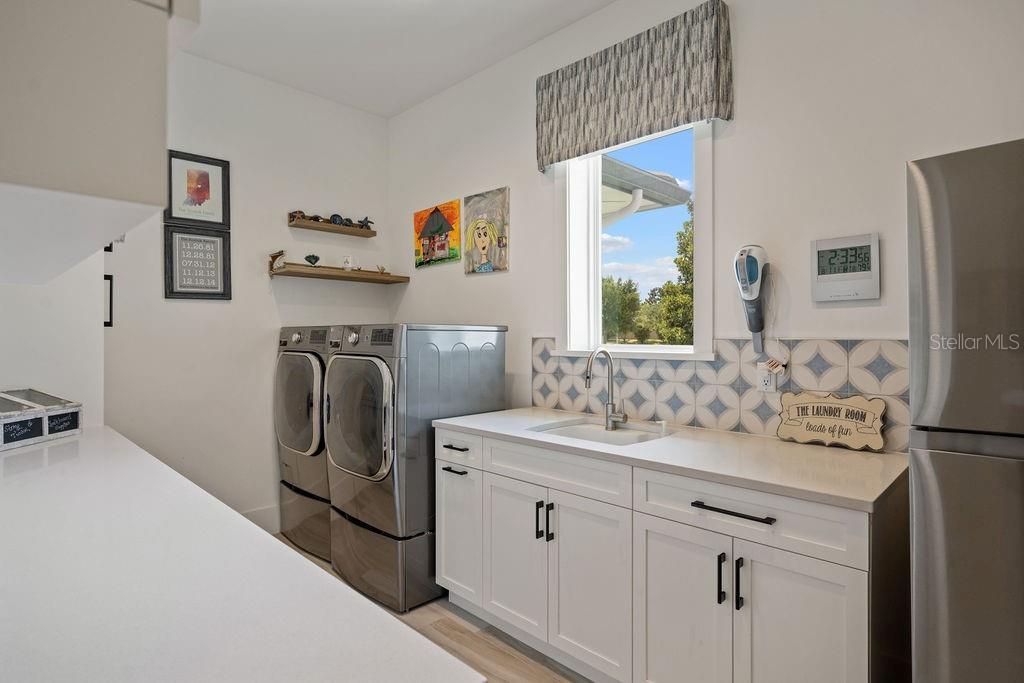 Oversized laundry room 14'.5" x 8' is equipped with custom cabinetry, sink, folding counter space and a window to provide natural light.