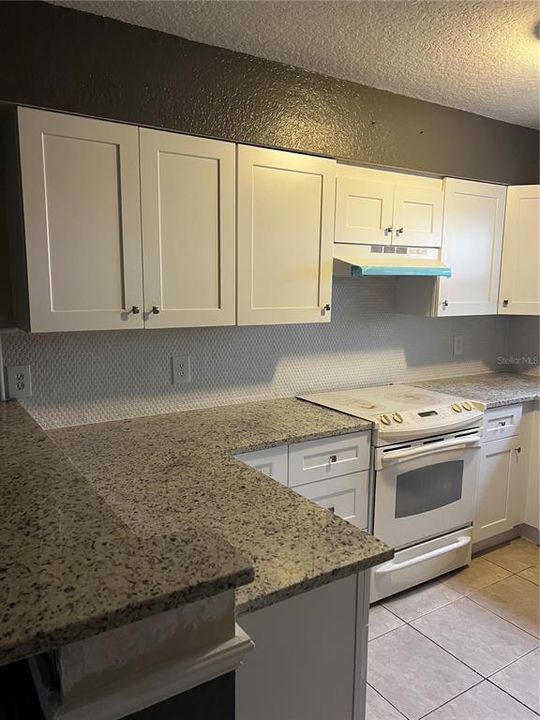 New remodeled kitchen with backsplash, hood, granite countertops and white cabinets.