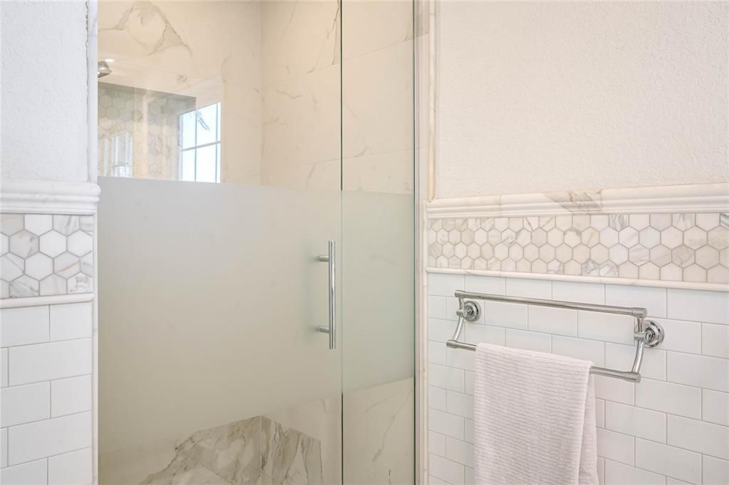 The spa like shower features a partially frosted door and beautiful tile.
