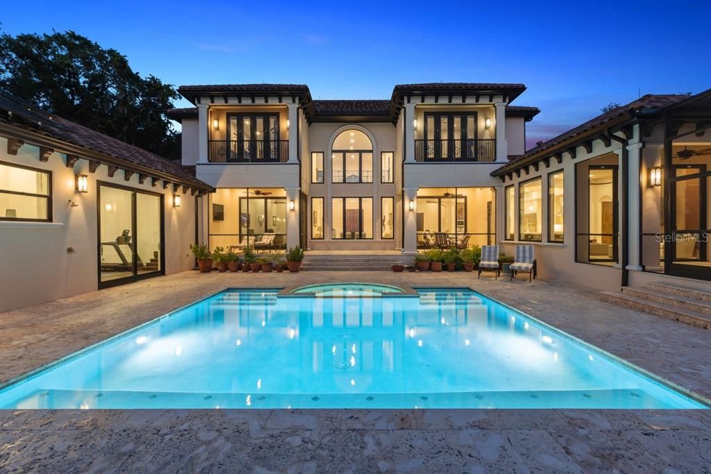 Majestic home's back exterior with a tranquil pool and warm lighting, inviting serene evenings.