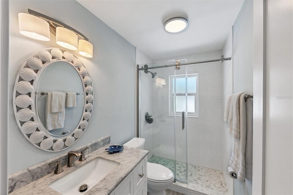 Guest Bathroom features walk-in shower with designer tile and Euro Glass door, in addition to beautiful coastal vanity with marble countertop.