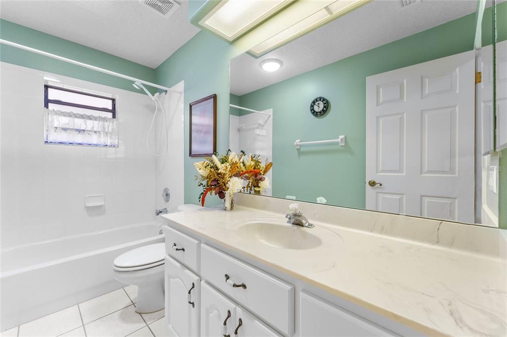 Guest bath has solid counter, a tub/shower combo, a window and an exhaust fan