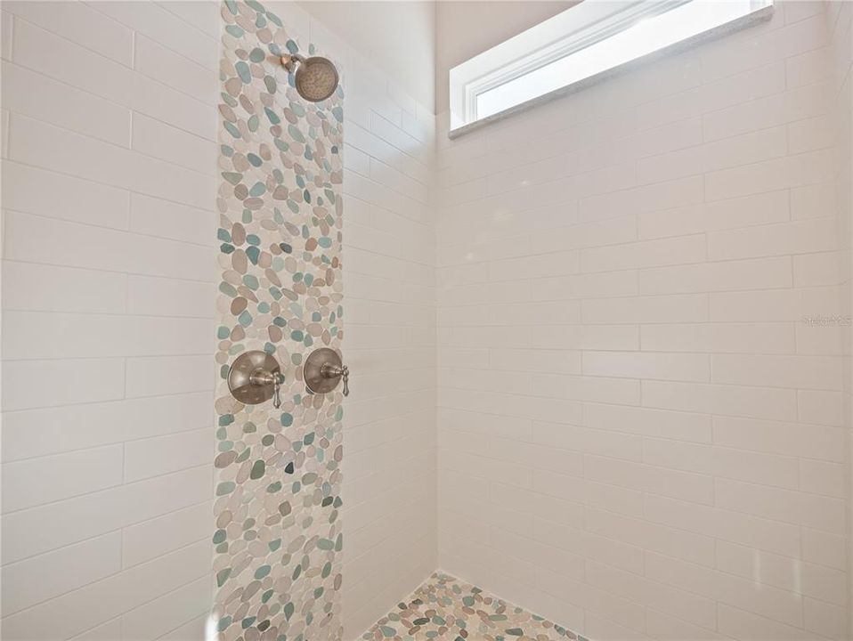 Primary bathroom shower with beautiful stone work, and dual shower heads. Natural light.