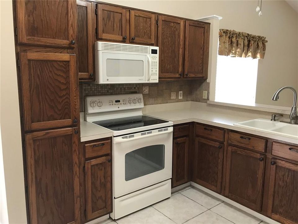 U-shaped kitchen opens with a serving bar to family room.  Notice abundant cabinets and glass cooktop with five burners.