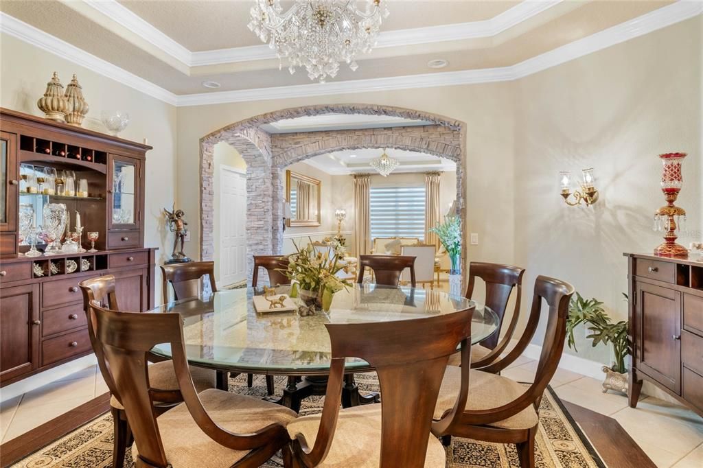 Dining room looking into gallery and formal living. Notice the wood inlay and stone floors mirrored by tray ceiling with crown molding. The impressive arched stone columns and entryways add a sense of old world charm to the formal spaces.