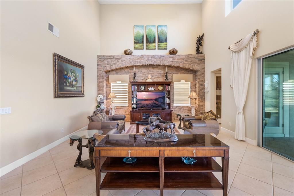 Family room- A soaring 21 FT ceiling, custom entertainment center, large picture windows above the wall of sliders, and full pool bath (through the entryway far right), add comfort and complement this space. This space is much larger than the image portrays.
