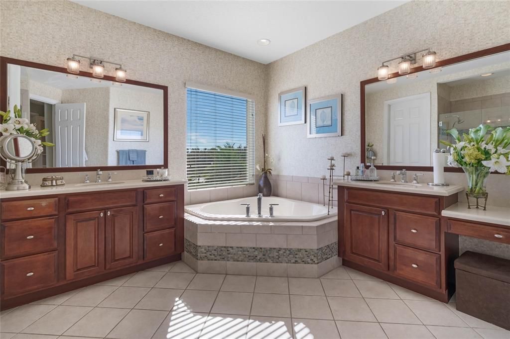 Primary ensuite bath featuring two granite topped vanities, corner soaking tub, separate glass enclosed shower and water closet.