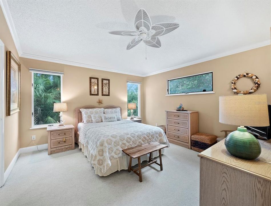 Enjoy the luxury of your main floor primary bedroom, a haven of relaxation just steps away from the heart of the home, adorned with large windows, offering green vistas of lush vegetation.