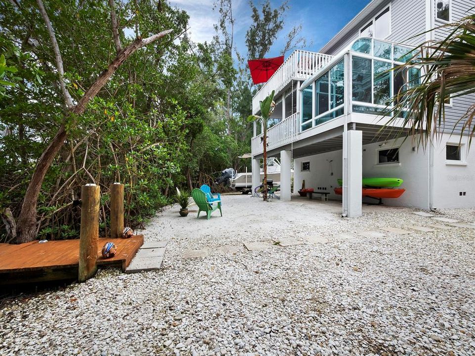 Coastal paradise at your doorstep: the back of your home opens to a sandy beach area, featuring a covered outdoor shower, kayak storage, and a dock extending to the tranquil bayou.