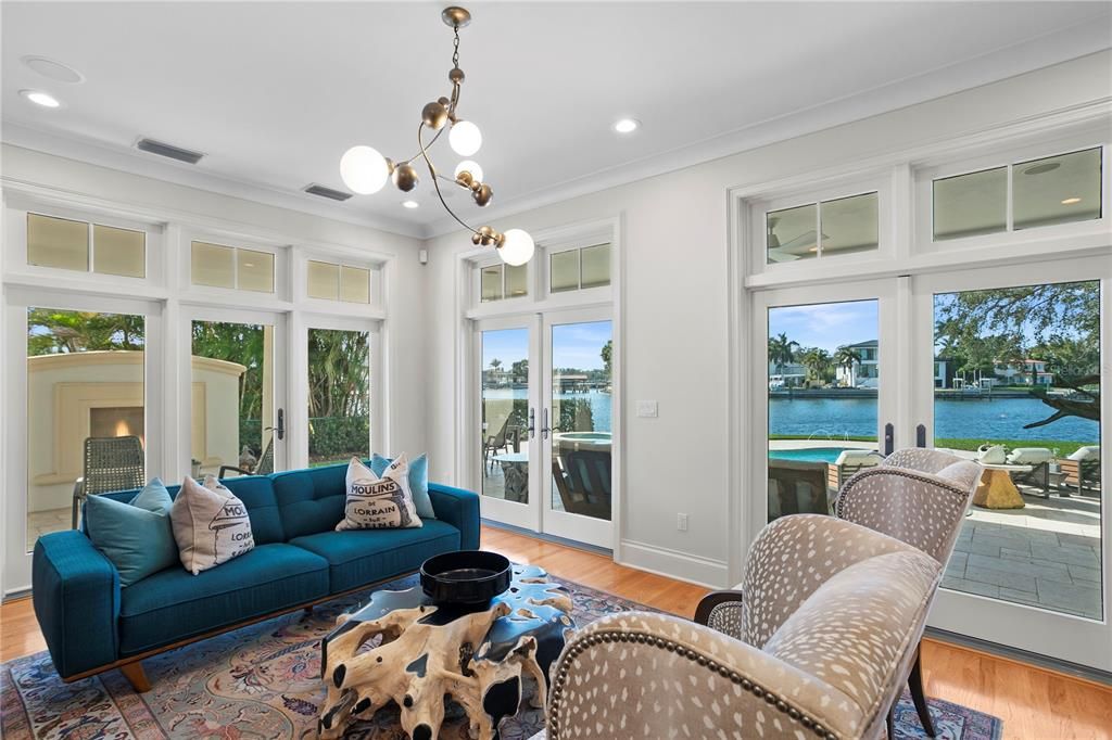 Main level sitting room with water views and access to outdoor cozy fireplace, outdoor dining and beautiful pool.