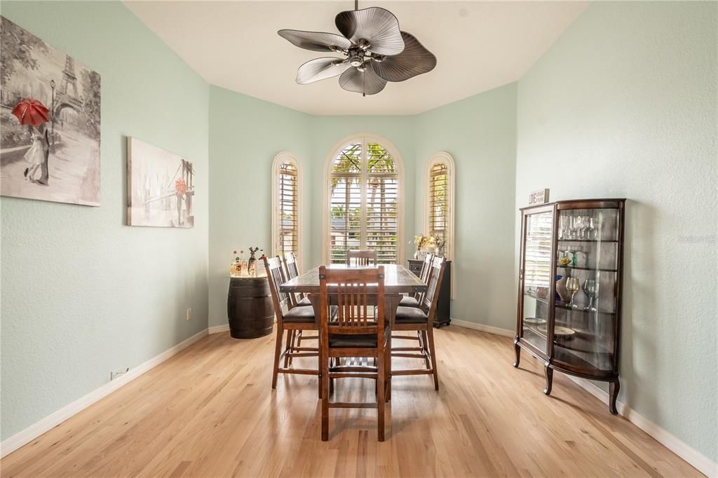 The dining room features a wood floor, plantation shutters, a bay window and ceiling fan.
