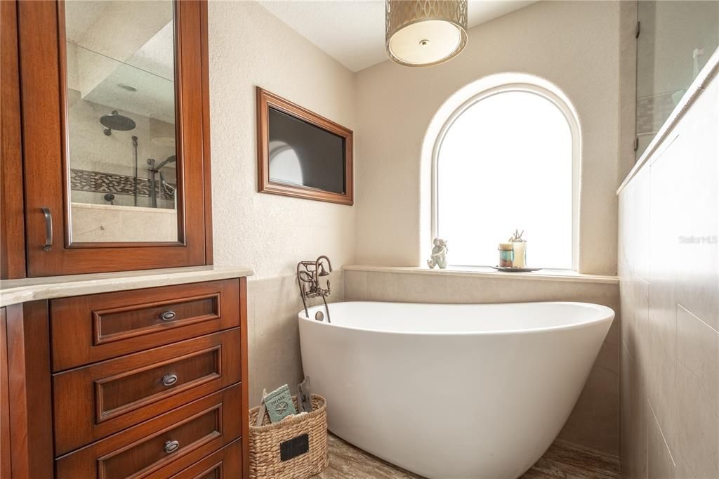The primary en-suite features a soaking tub with a framed flat screen tv above.