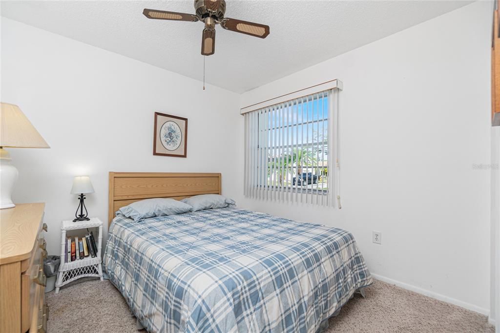 The guest bedroom has carpeted flooring and a ceiling fan.