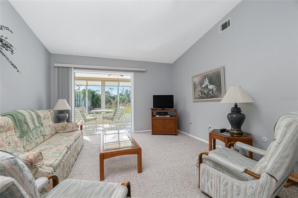 The living room has carpeted flooring, a ceiling fan and sliding glass doors to the Florida room.