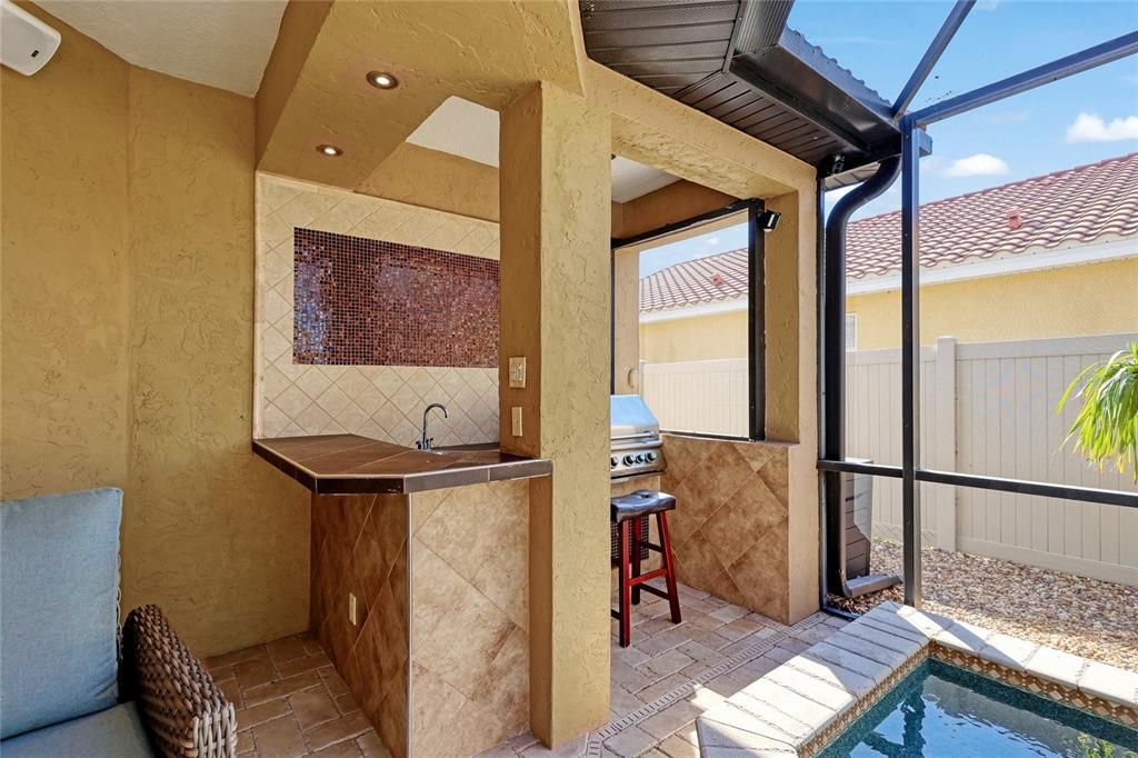 Covered outdoor Kitchen with Grill, new Refrigerator and sink with custom tile backsplash.