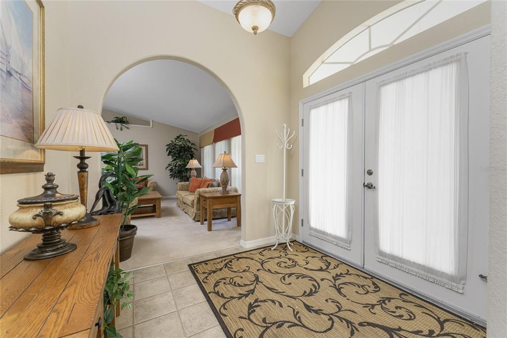 The bright and airy foyer has glass panel, double front doors, an arched transom window above, and added lighting.