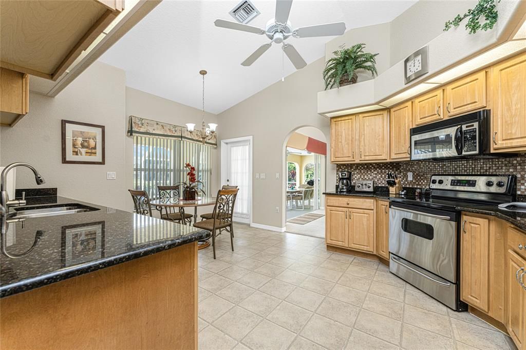 The spacious kitchen has wood cabinetry with granite counter tops and a ceiling fan.