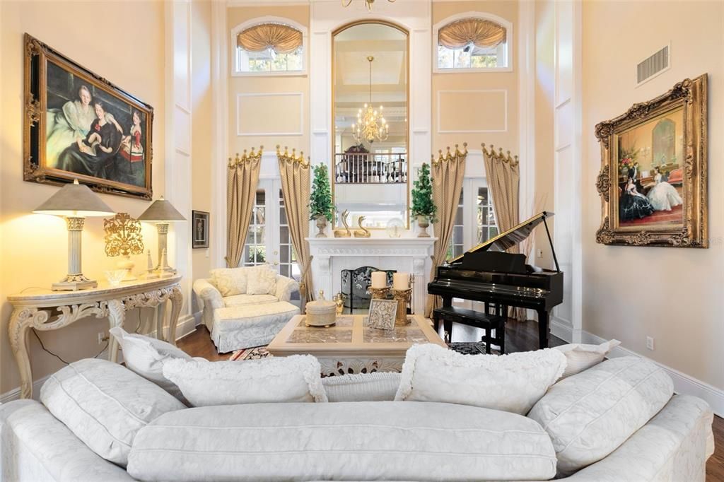 The formal living room, with its soaring two-story ceiling, fireplace, and dual French doors, serves as a focal point for sophisticated gatherings.