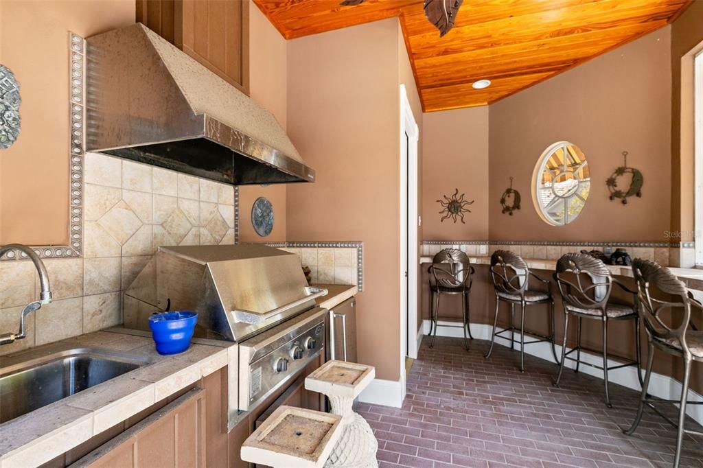 It includes a summer kitchen with a grill, fridge and bar seating.