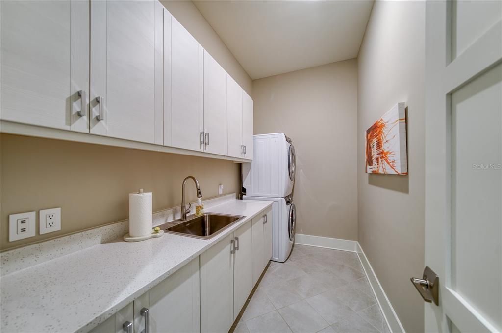 Laundry room has additional cabinetry, front load steam washer with dryer, porcelain tile flooring.