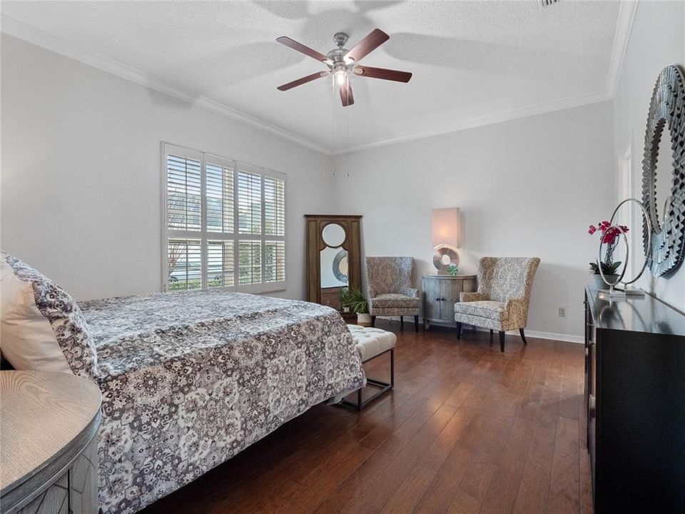 Primary bedroom with wood floors, crown molding, and ceiling fan