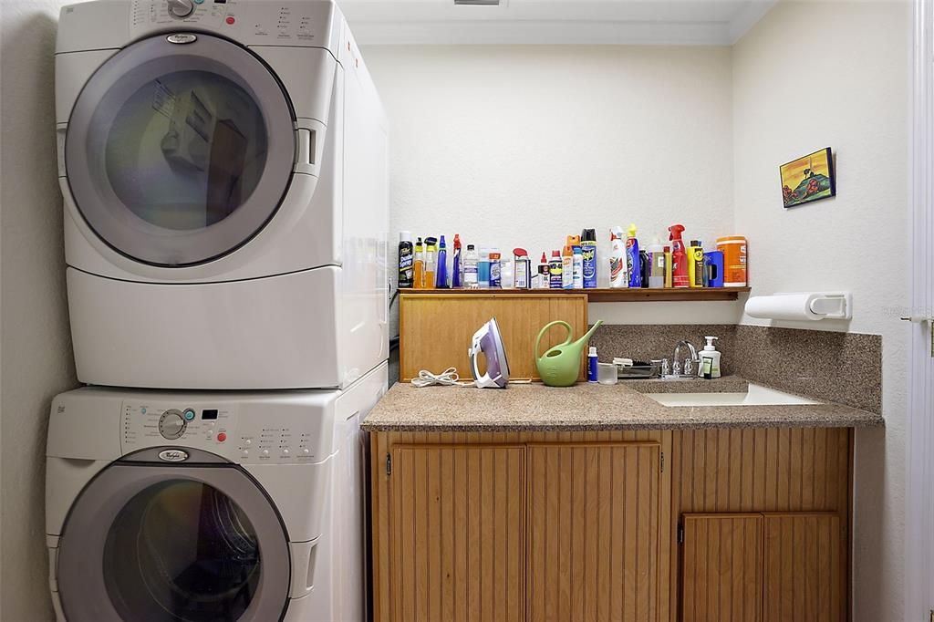 inside laundry room with stackable washer and dryer (included) and utility sink with storage