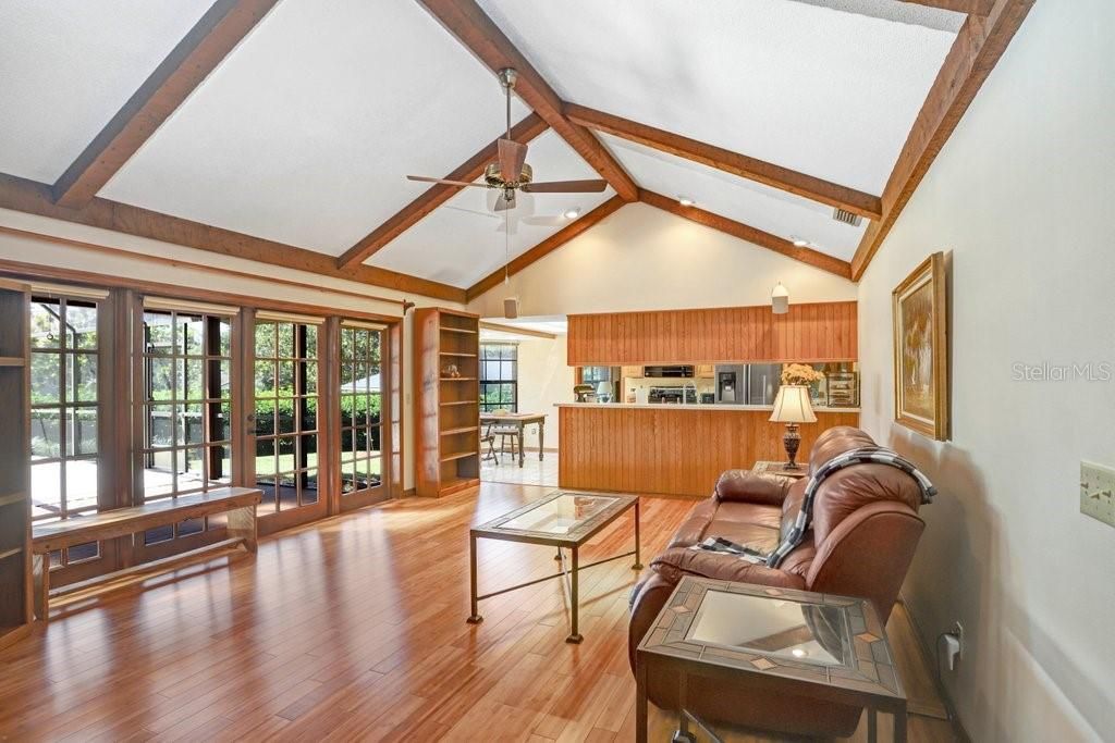 The wide open family room features wooden ceiling beams, a brick fireplace, hardwood floors, and beautiful french doors to the screened-in pool lanai.