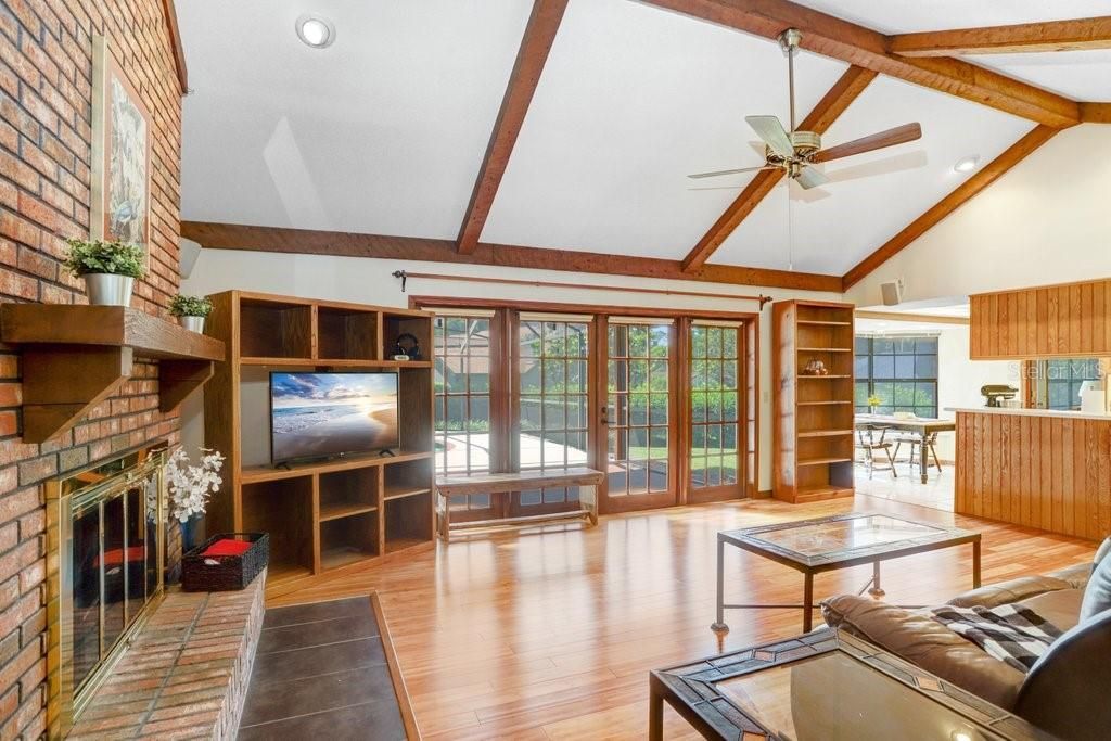 As you walk straight ahead, you'll find the wide open family room that features wooden ceiling beams, a brick fireplace, hardwood floors, and beautiful french doors to the screened-in pool lanai.