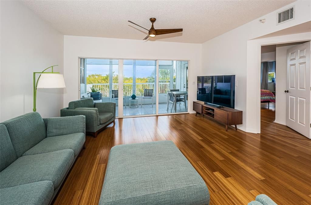 Bright and open living room featuring bamboo flooring and triple slider to lanai and balcony.