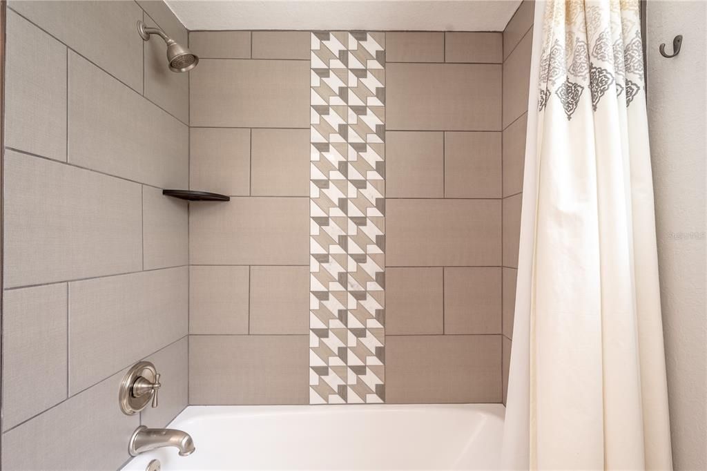A tub with shower with artistic accent tile in the upstairs full bath.