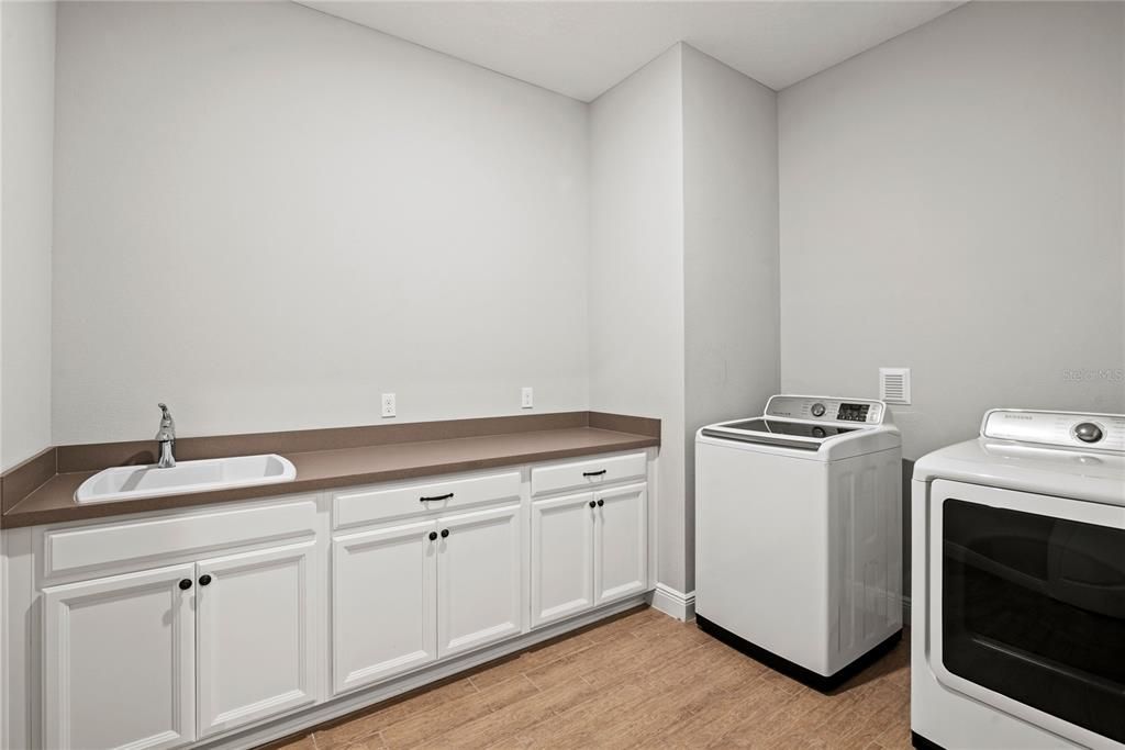 Spacious main level laundry room with mud sink and plenty of counter and cabinet space for additional storage. Washer and dryer convey in sale.