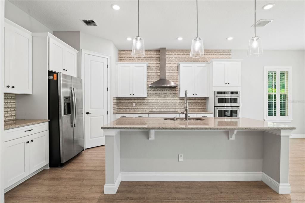 Spacious chef's kitchen features granite counters, 42" cabinets with crown molding, custom backsplash extending to ceiling, stainless steel Kitchen Aid appliances, walk in pantry with custom shelving and large center island with breakfast bar overlooking Family Room