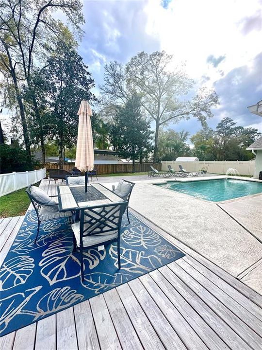 Outdoor dining area on deck overlooking pool and fenced backyard