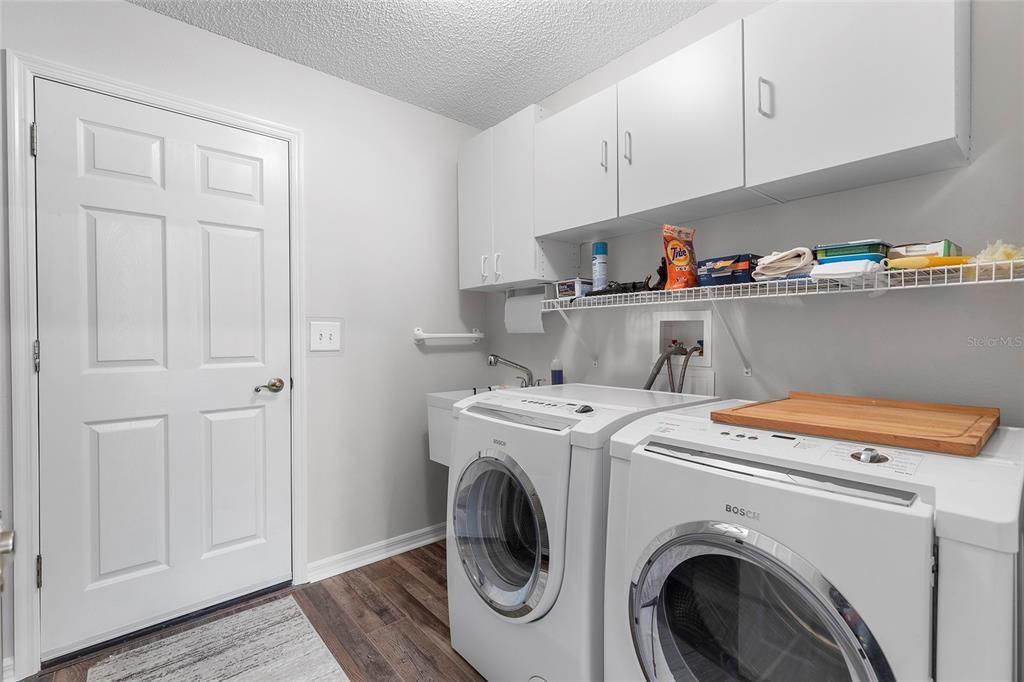 Inside laundry room with overhead cabinets, laundry tub and door leading to garage.