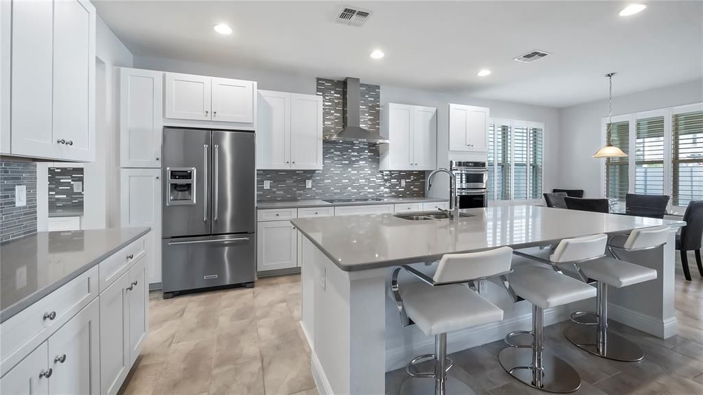 Kitchen with large center island, breakfast bar, walk-in pantry, eat-in breakfast nook, stainless steel appliances, quartz countertops, and custom back splash.