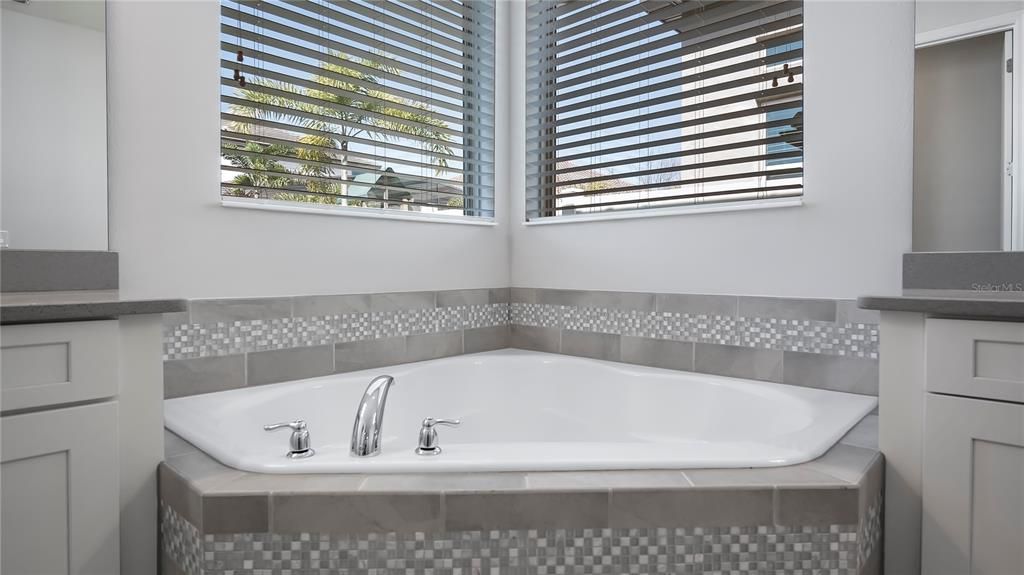 Primary spa-like en-suite with large corner soaking tub, walk-in shower, quartz countertops, and double vanities.