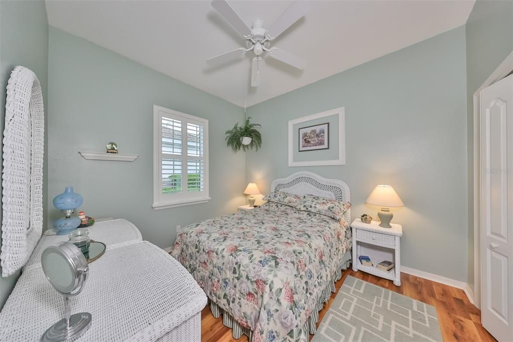 Plantation shutters accent this room, with a ceiling fan and soft coastal colors, in this light and bright guest bedroom.