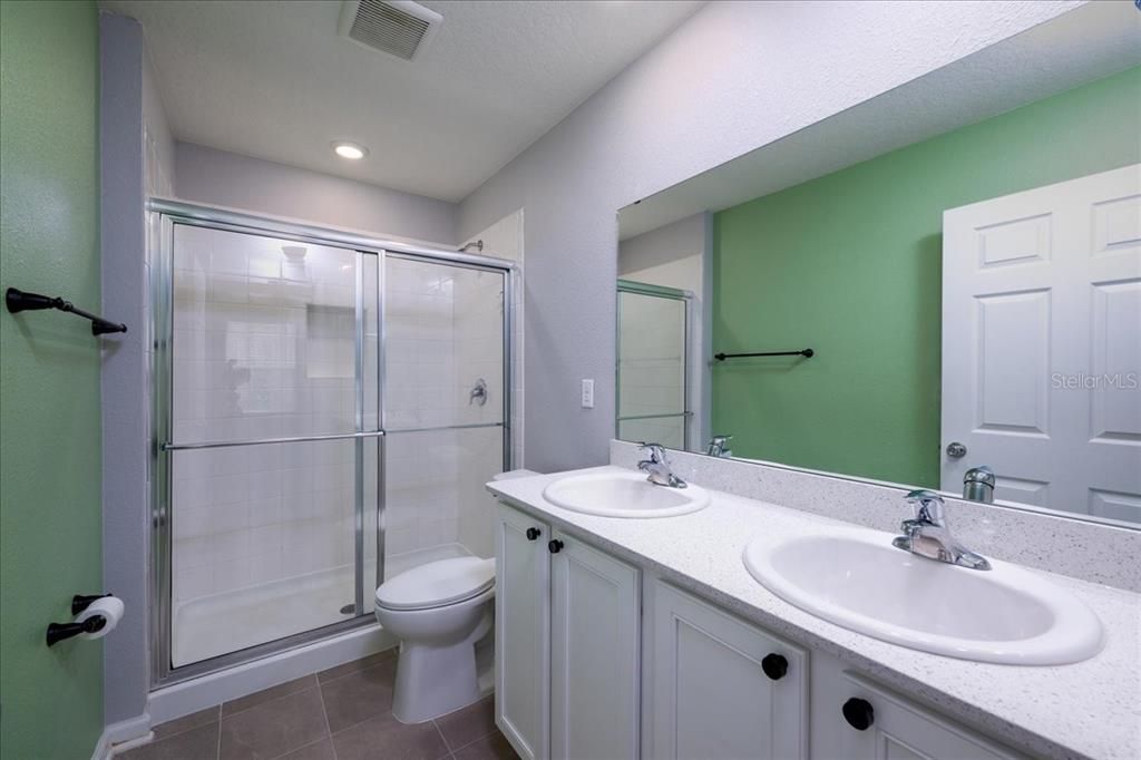 Walk-in shower, with dual sinks also sitting on quartz countertops.