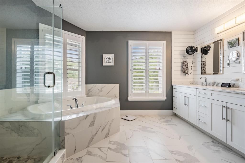 Primary bathroom with marble counter tops, ship lap walls, new fixtures and cabinets, flooring and plantation shutters.