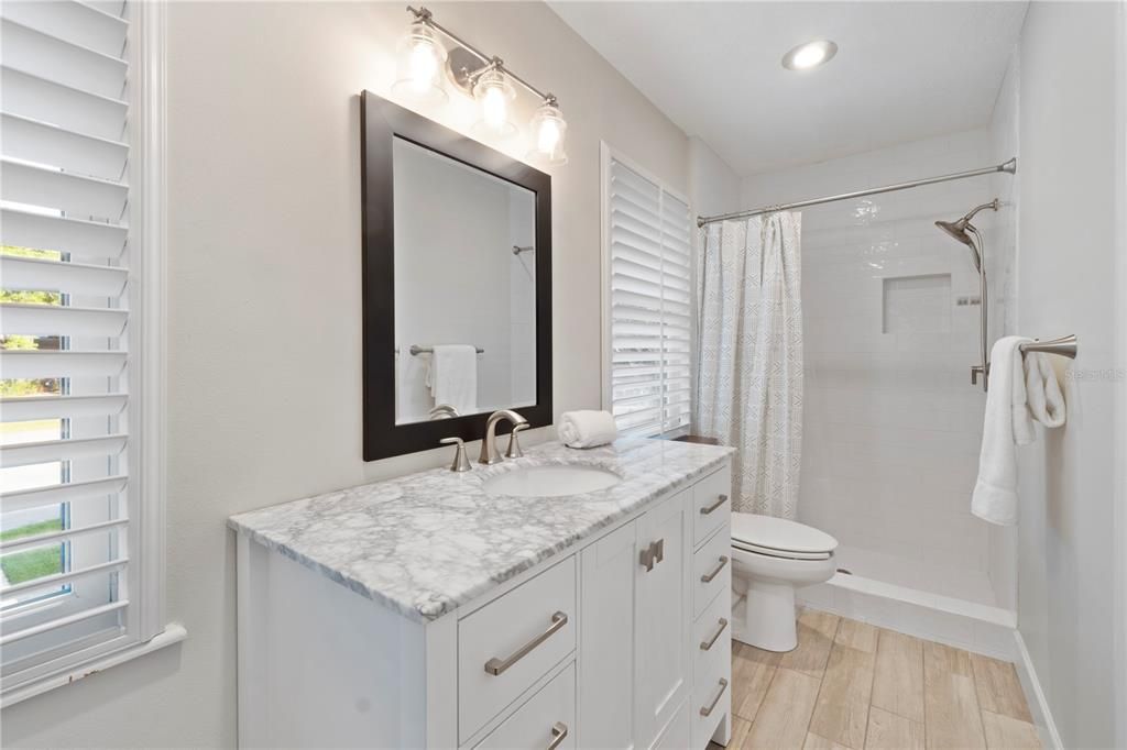 The ensuite bathroom for Bedroom 2 features wood-tiled floors, offering depth and warmth that beautifully complement the pristine white subway tile in the shower.