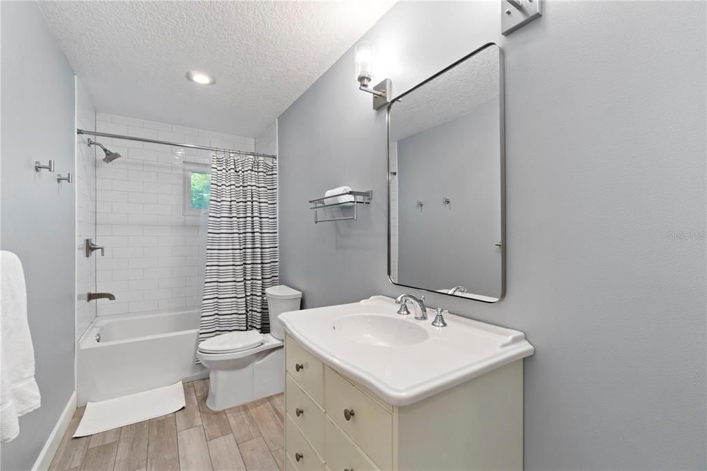 The upstairs full bathroom showcases wood-tiled floors that add depth and warmth, perfectly complementing the pristine white subway tile in the bath and shower.