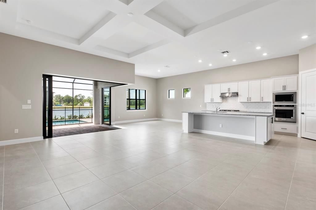 Open living area with coffered ceiling and corner sliding doors alongside the kitchen and dining area, all overlooking the beautiful pool and lake.