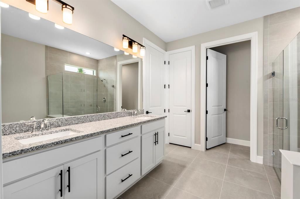 Tile flooring, granite counters with dual sinks, linen closet, water closet and walk-in shower in the primary bathroom.