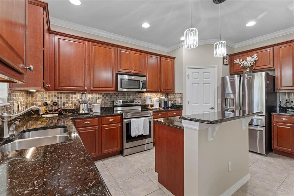 The island kitchen features stainless appliances, granite counters and solid wood cabinetry. The door toward the back leads to a generous walk-in pantry. To the right of the refrigerator lies a beverage bar.