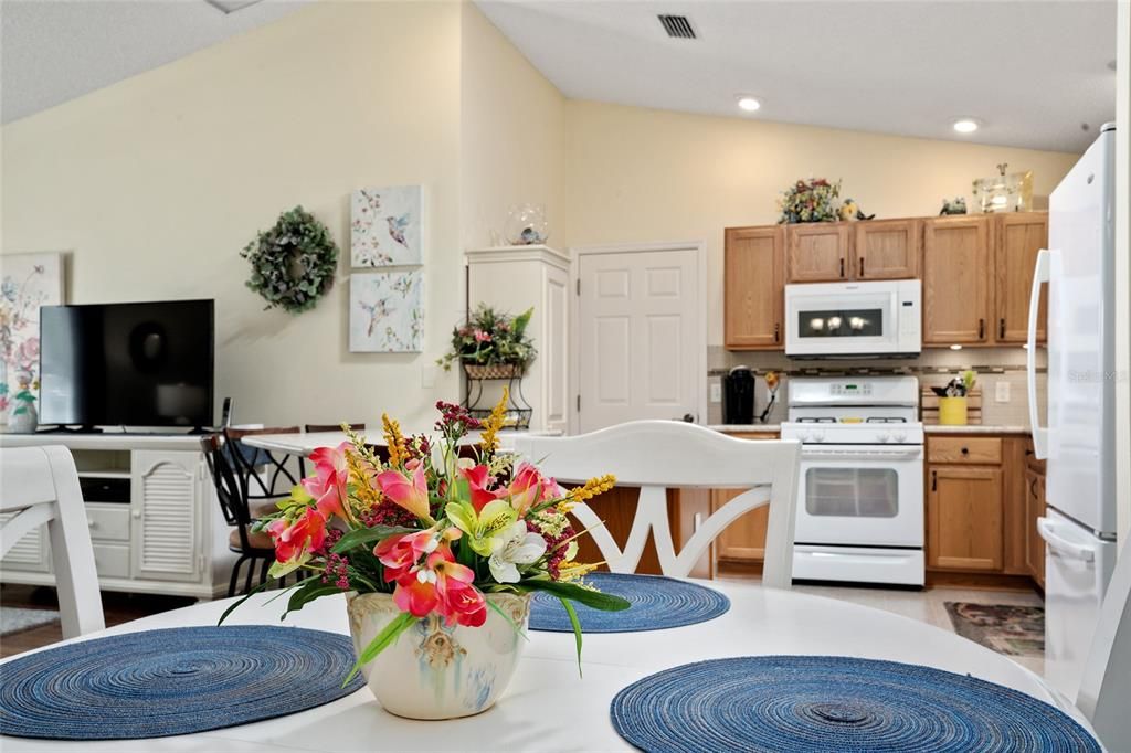 View of DINING ROOM shows colorful, fresh flowers as table centerpiece. KITCHEN (back R) shows custom white, stand alone PANTRY (back L against wall) & exit door to GARAGE (back center).