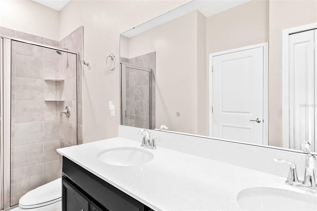 Primary Bathroom with walk in shower, dual vanity sinks, and quartz countertops