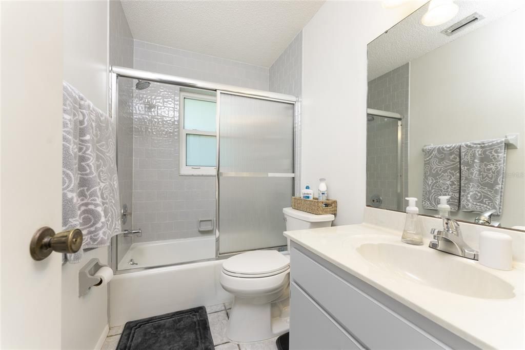 Guest bathroom has tiled floor, a combo tub/shower with door, and a vanity with a cultured marble top.